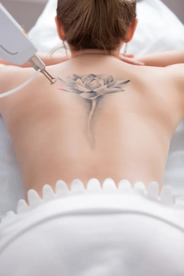 The back of the woman laid on bed with black lotus tattoo between scapulas.