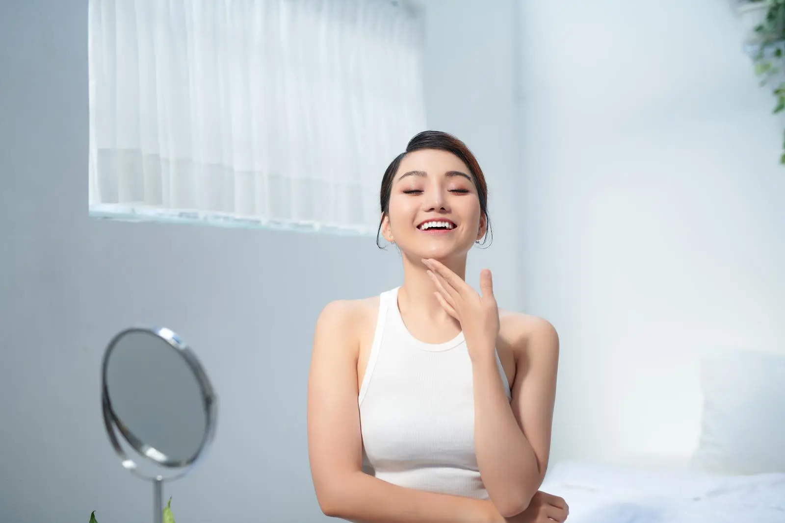 The woman has a happy face and is touching her chin with her hand in a white room.